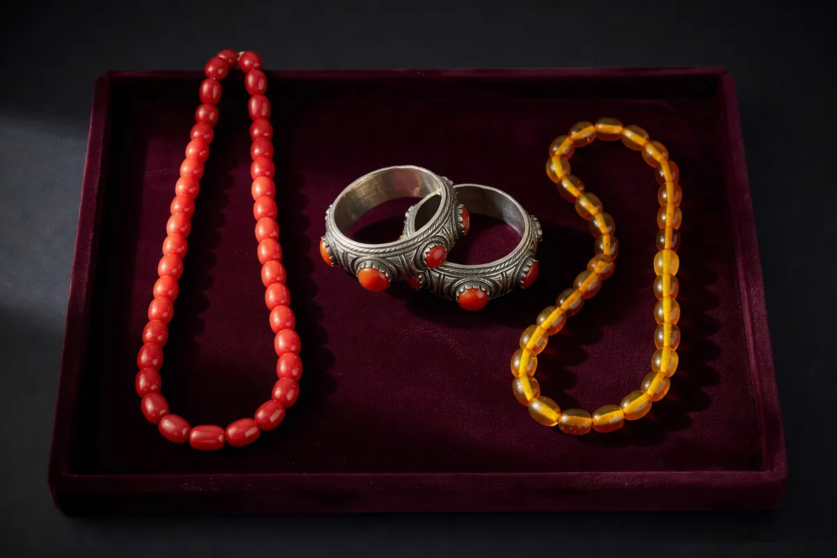 Sautoir de corail, bracelets d'argent incrustés de cornaline et collier d'ambre posés sur un plateau de velours sombre